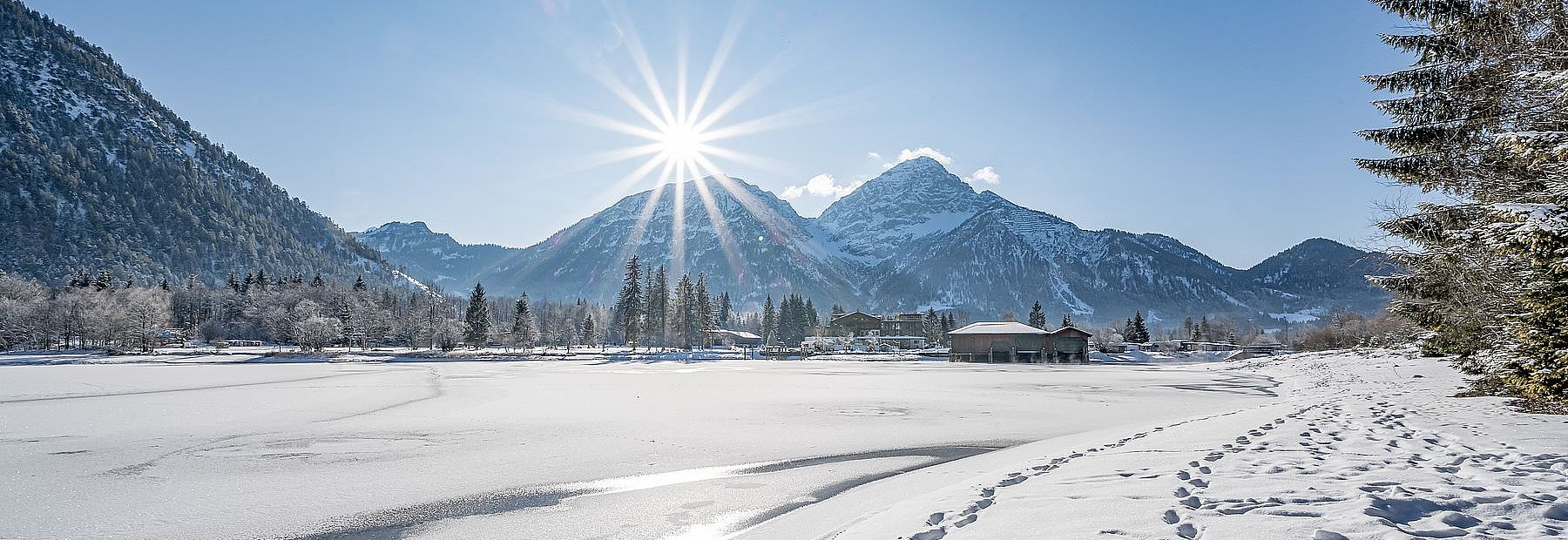 Verschneiter Heiterwanger See im Winter mit Blick auf das Hotel Fischer am See bei Sonnenschein